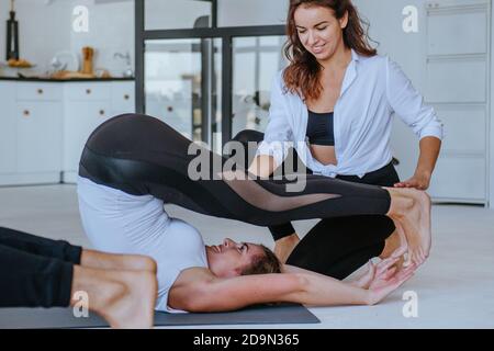 Yoga-Coach hilft jungen Frauen Yoga-Pose üben. Yoga-Gruppenkurs für Erwachsene. Stockfoto