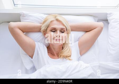High-Winkel-Ansicht Foto von überglücklich im Alter Dame Frau entspannend Aufwachen liegend weiße Bettwäsche heimelige Schlafzimmer drinnen Stockfoto