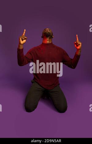 Afrikanischer Mann auf Knien zeigt und schaut nach oben. Vorderansicht. Isoliert. Volle Länge. Stockfoto