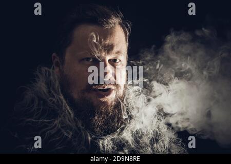 Fester bärtiger Mann in einem Pelzmantel, der Dampf ausatmet Aus seinem Mund Studio Porträt Stockfoto