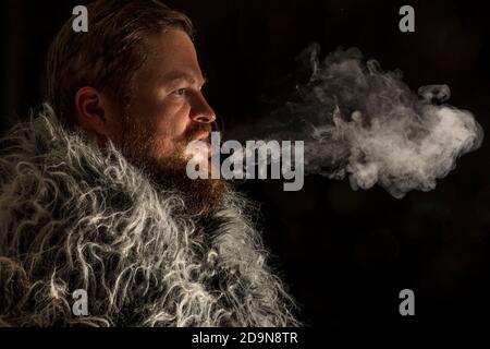 Fester bärtiger Mann in einem Pelzmantel, der Dampf ausatmet Aus seinem Mund Studio Porträt Stockfoto