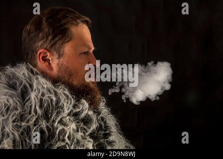 Fester bärtiger Mann in einem Pelzmantel, der Dampf ausatmet Aus seinem Mund Studio Porträt Stockfoto