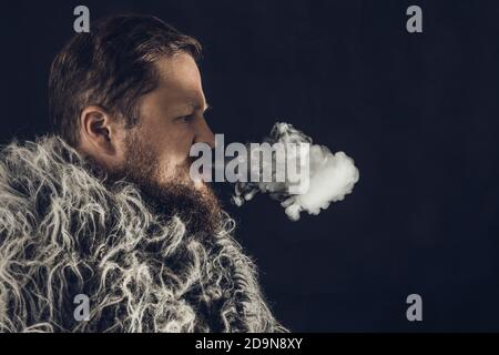 Fester bärtiger Mann in einem Pelzmantel, der Dampf ausatmet Aus seinem Mund Studio Porträt Stockfoto