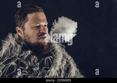 Fester bärtiger Mann in einem Pelzmantel, der Dampf ausatmet Aus seinem Mund Studio Porträt Stockfoto