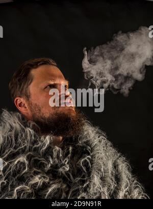 Fester bärtiger Mann in einem Pelzmantel, der Dampf ausatmet Aus seinem Mund Studio Porträt Stockfoto