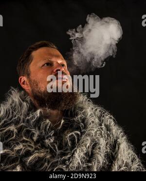 Fester bärtiger Mann in einem Pelzmantel, der Dampf ausatmet Aus seinem Mund Studio Porträt Stockfoto