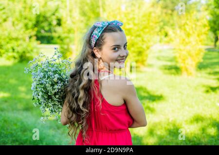 Zeit für Abenteuer. Glückliches Mädchen lächeln mit Blumen auf natürliche Landschaft. Erholung im Freien. Sommerurlaub. Reisen und Fernweh. In die Wildnis. Das Leben ist ein gewagtes Abenteuer. Stockfoto