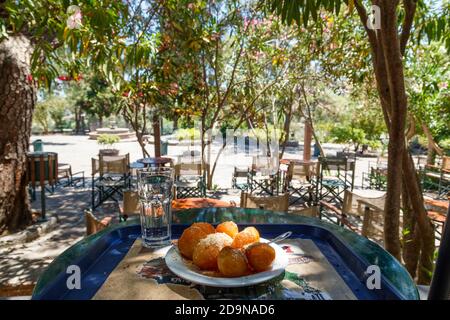 Loukoumades, das sind griechische traditionelle Donuts, die auf einem weißen Teller entlang einer Vase mit kühlem Wasser serviert werden, wie sie im Kloster von Taksiarchis auf Lesvos serviert werden Stockfoto