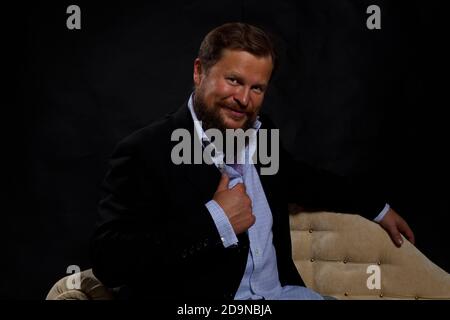 Smilingl solider bärtiger Mann in Anzug auf dem Sofa sitzend studio Porträt auf schwarzem Hintergrund Stockfoto