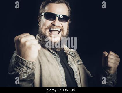 Emotionaler bärtiger Mann in Sonnenbrille in Lederjacke gekleidet ist Glücklich, Studio Portrait zu gewinnen Stockfoto