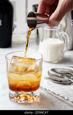 Menschenhand gießt Kaffeelikör in ein Glas mit Eis. Weiße russische Cocktail-Zubereitung Stockfoto