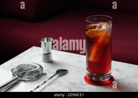 Americano Cocktail mit Orange Twist auf einem Marmortisch. Rotes Sofa als Hintergrund Stockfoto