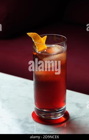 Americano Cocktail mit Orange Twist auf einem Marmortisch. Rotes Sofa als Hintergrund Stockfoto