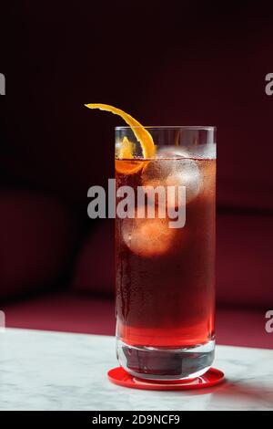 Americano Cocktail mit Orange Twist auf einem Marmortisch. Rotes Sofa als Hintergrund. Vorderansicht Stockfoto