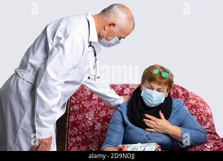 Ein alter ernsthafter Arzt mit Maske überprüft das Wohlbefinden einer älteren Frau bei einer ärztlichen Untersuchung zu Hause. Virus- und Pandemiekonzept Stockfoto