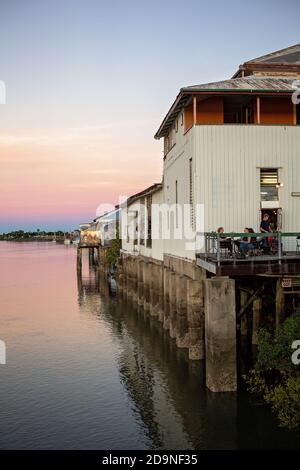 Mackay, Queensland, Australien - 12. Juli 2019: Menschen essen auf der Außenterrasse und weiter unten im beleuchteten Wharf Restaurant am Wasser bei Sonnenuntergang Stockfoto