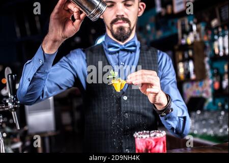 Der erfahrene Barkeeper verleiht einem Getränk den letzten Schliff In der Bar neben dem Tresen stehen Stockfoto