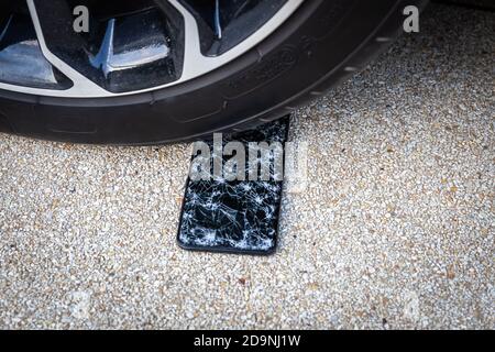 Unter dem Autorad mit verlorenem modernen Smartphone fallen Fiel mit rissiger Glasscheibe Stockfoto