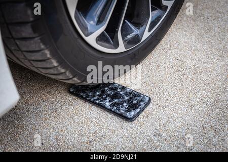 Unter dem Autorad mit verlorenem modernen Smartphone fallen Fiel mit rissiger Glasscheibe Stockfoto