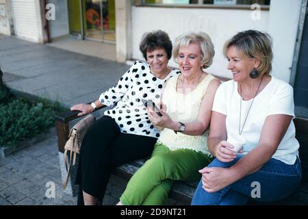 Reife Frauen lächeln auf dem Handy sitzen auf einem Bank Stockfoto