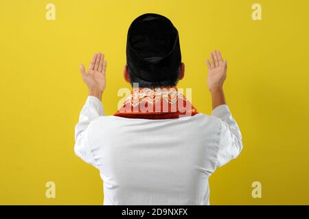 Junger asiatischer muslim, der die Hand hebt und betet, Rückansicht, isoliert auf gelbem Hintergrund Stockfoto