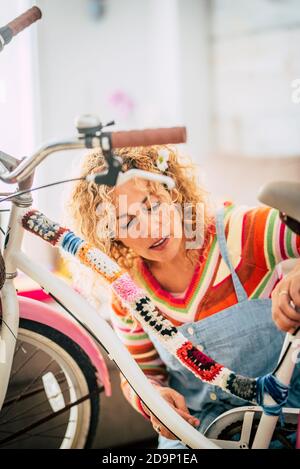 Glückliche Erwachsene Frau zu Hause in Hobby Arbeit Freizeit Tätigkeit Indoor ändern Sie ein weibliches Fahrrad mit Stück Abdeckungen und Voller Farben - Kreativitätskonzept und hippiges Boho-Fahrrad Kreation - Menschen genießen künstlerische Arbeit zu Hause Stockfoto