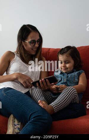 Eine Mutter mit ihrer Tochter gucken friedlich ein Video auf Ein Telefon, während man auf dem Sofa sitzt Stockfoto