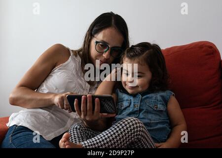 Eine Mutter mit ihrer Tochter gucken friedlich ein Video auf Ein Telefon, während man auf dem Sofa sitzt Stockfoto