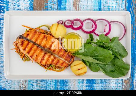 Köstliche gekochte Lachsfischfilets. Ein Stück gebackenen Lachs gegrillte Pfeffer Zitrone und Salz auf einem weißen Teller mit Salatblättern. Holzhintergrund. Stockfoto