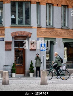 Lund, Schweden - 10. Oktober 2020: Junger Mann fotografiert vor einem mittelalterlichen Gebäude, während der Student an der Universität vorbei radelt Stockfoto
