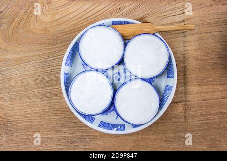Thai Kokosmilch Pudding ist ein thailändisches Dessert aus Reismehl, Kokosmilch und Zucker der kleine Keramik Tassen sind auf einem Holzboden. Khano Stockfoto