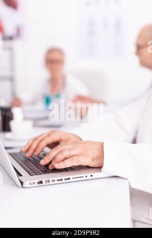 Nahaufnahme der Hände des Arztes beim Tippen auf der Laptop-Tastatur während des Treffens mit seinem medizinischen Team. Klinik Experte Therapeut im Gespräch mit Kollegen über Krankheit, medizinische Fachkraft Stockfoto