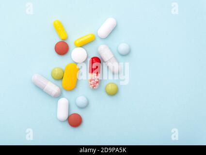 Medizinische Zusammensetzung. Einige Farbtabletten auf blauem Hintergrund, Draufsicht. Gelbe, blaue, grüne, rote, weiße Kapseln, Medikamente. Stockfoto