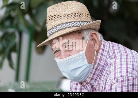 Älterer Mann mit Strohhut trägt eine Gesichtsschutzmaske aufgrund der globalen Pandemie des Coronavirus, covid 19. Stockfoto