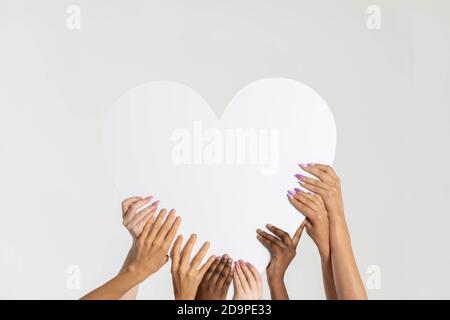 Herzform durch weibliche Hände gehalten. Viele Frauen aus verschiedenen Ländern haben ein gemeinsames Herz in einer Geste der Einheit. Stockfoto