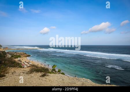 Eine Weitwinkelaufnahme am Pandawa Beach, Bali mit Sonnenschirmen am Sandstrand mit starken Wellen am Meer und einem blauen Himmel Stockfoto