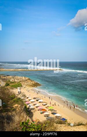 Eine Weitwinkelaufnahme am Pandawa Beach, Bali mit Sonnenschirmen am Sandstrand mit starken Wellen am Meer und einem blauen Himmel Stockfoto