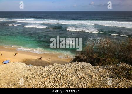 Eine Weitwinkelaufnahme am Pandawa Beach, Bali mit Sonnenschirmen am Sandstrand mit starken Wellen am Meer und einem blauen Himmel Stockfoto