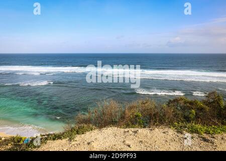 Eine Weitwinkelaufnahme am Pandawa Beach, Bali mit Sonnenschirmen am Sandstrand mit starken Wellen am Meer und einem blauen Himmel Stockfoto