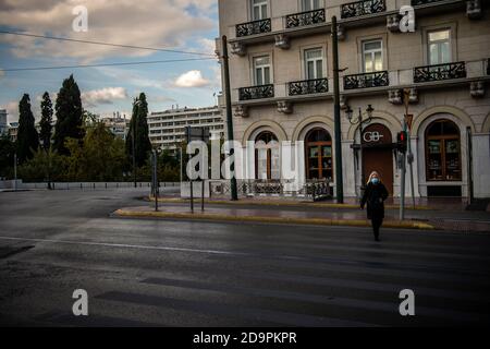 Athen, Griechenland. November 2020. Eine Frau mit Nasenmaul-Bedeckung überquert eine verlassene Straße. Seit Samstag, 07.11.2020, ist in ganz Griechenland eine dreiwöchige Sperre in Kraft. Ab 6.00 Uhr müssen alle Geschäfte außer Supermärkten, Apotheken und anderen wichtigen Geschäften geschlossen werden. Von 21.00 bis 5.00 Uhr gibt es eine Nachtruhe. Wer tagsüber einkaufen gehen oder einen Arzt aufsuchen möchte, muss die Behörden per SMS informieren. Masken sind überall Pflicht. Quelle: Angelos Tzortzinis/dpa/Alamy Live News Stockfoto