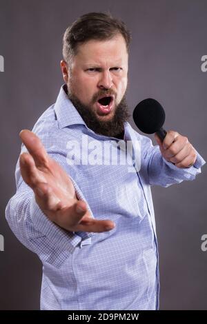 Bärtige emotionale Sängerin mit Mikrophon gekleidet in Hemd Studio Porträt Stockfoto