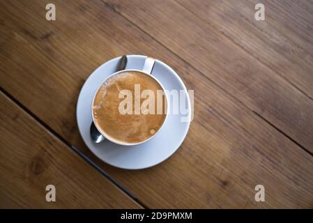 Flacher weißer Kaffee und Untertasse auf einem hölzernen Couchtisch - über Schuss Stockfoto