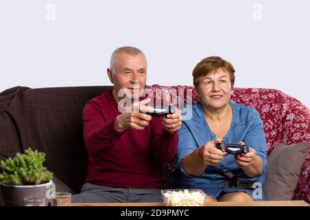 Ein Seniorenpaar spielt zu Hause eine Spielkonsole mit Joysticks und hat Spaß. Senior Online- und Pandemiekonzept. Stockfoto