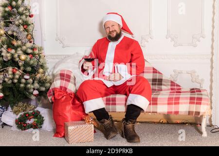 Bärtiger Mann im Weihnachtsmann Kostüm sitzend auf dem Sofa Mit einem Glas Wein Studio Porträt Stockfoto