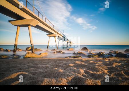 Schöner Pier am Badalona Strand in der Nähe von Barcelona, Spanien. Sonnenuntergangsfarben und kräftige Wellen Stockfoto