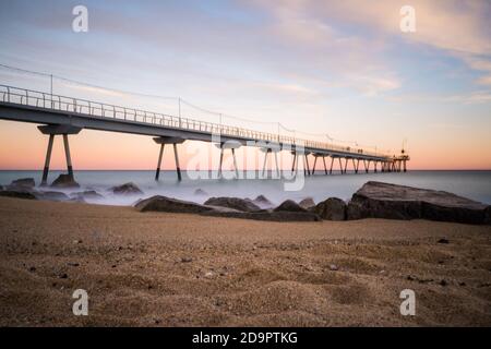 Schöner Pier am Badalona Strand in der Nähe von Barcelona, Spanien. Sonnenuntergangsfarben und kräftige Wellen Stockfoto