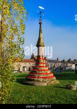 Der Markt aus dem 12. Jahrhundert kreuzt auf Norham Dorf grün in roten Mohnblumen für Remembrance Day, Norham, Northumberland, England dekoriert Stockfoto