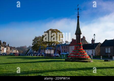 Der Markt aus dem 12. Jahrhundert kreuzt auf Norham Dorf grün in roten Mohnblumen für Remembrance Day, Norham, Northumberland, England dekoriert Stockfoto