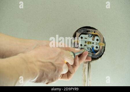 Installationsdraht in einen Stecker. Ein Mann installiert eine Steckdose in der Wand. Nahaufnahme des Technikers, der den Schraubendreher in der Nähe der Steckdose hält. Elektrisch Stockfoto