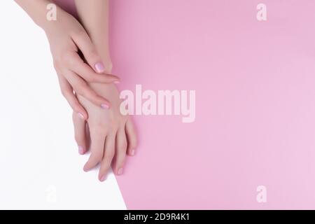 Schöne Damenhände mit einer stilvollen rosa Maniküre auf einem rosa und weißen Hintergrund. Stockfoto
